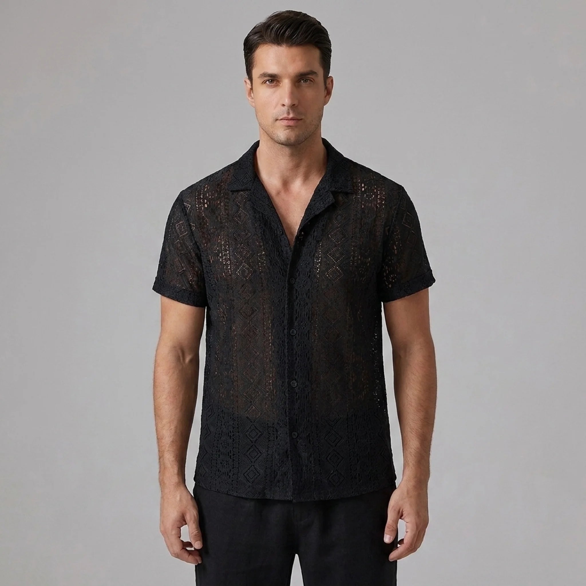 Three quarter view of man in black geometry textured Cuban shirt and linen pants on plain background