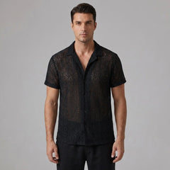 Three quarter view of man in black geometry textured Cuban shirt and linen pants on plain background