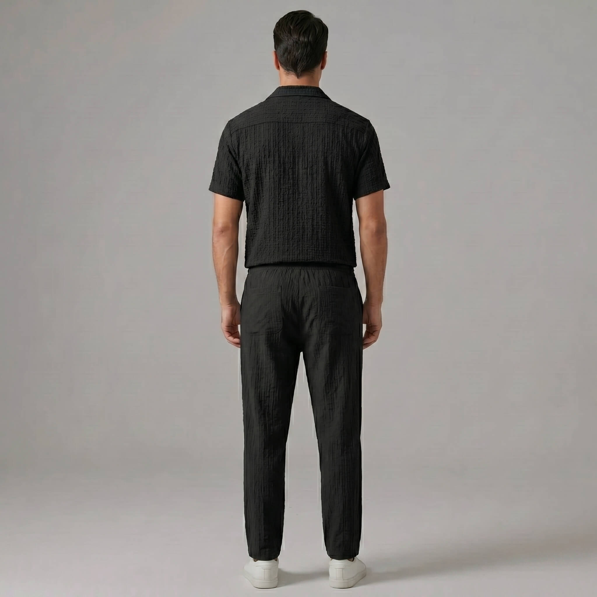 Back view of man wearing black jacquard Cuban collar shirt and crinkle textured straight leg pants