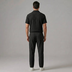 Back view of man wearing black jacquard Cuban collar shirt and crinkle textured straight leg pants