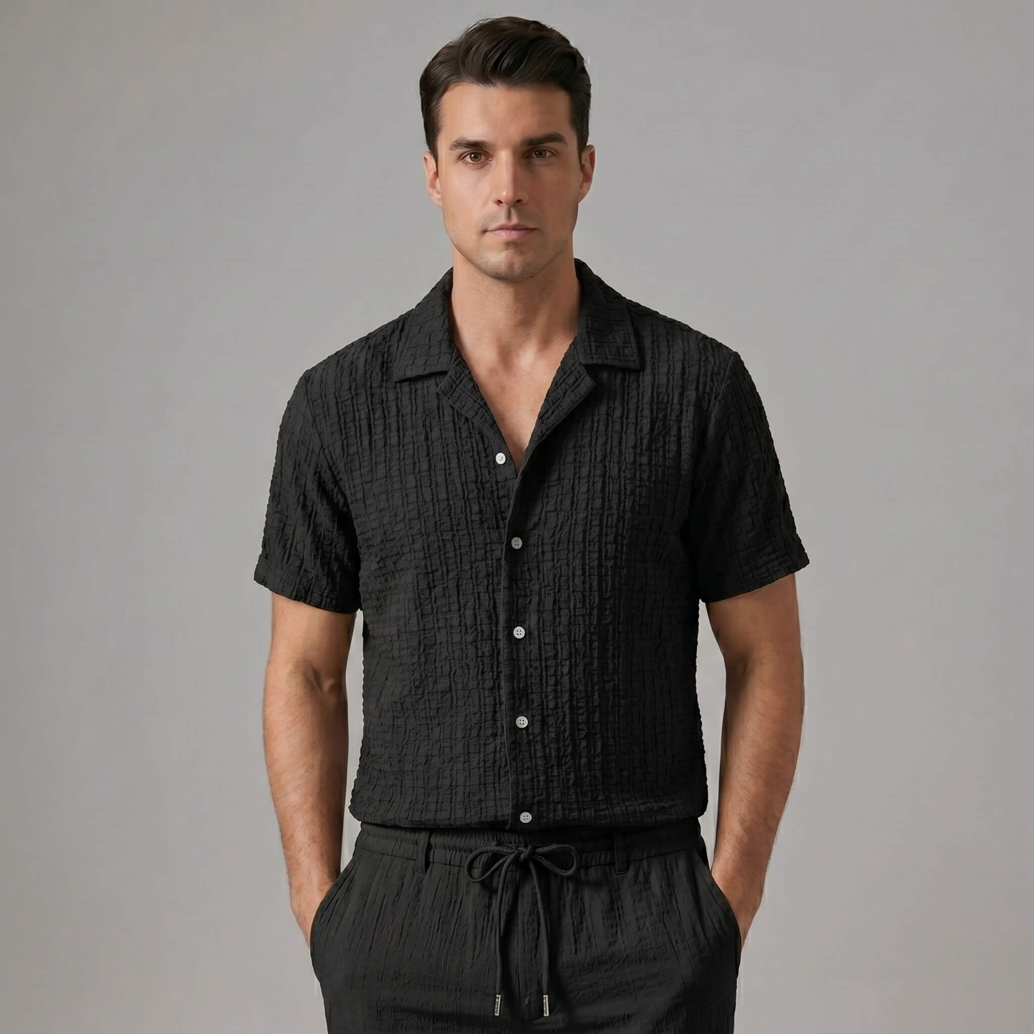 Three quarter view of man in black jacquard Cuban shirt and crinkle pants on white background