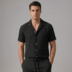 Three quarter view of man in black jacquard Cuban shirt and crinkle pants on white background