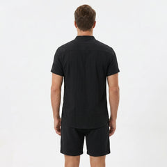 Back view of man wearing black linen look stand collar shirt and crinkle drawstring shorts