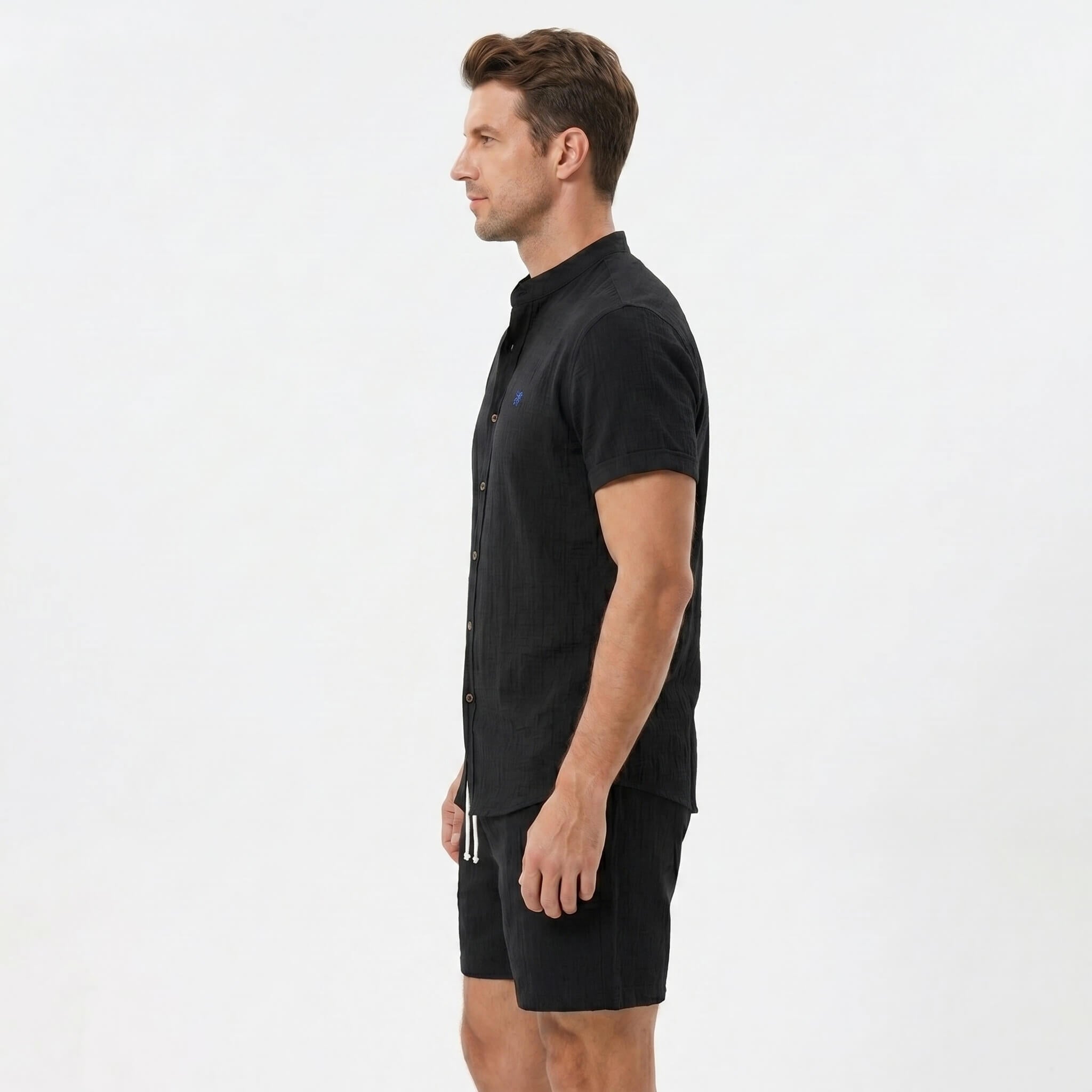 Side view of man in black linen look stand collar shirt and crinkle textured drawstring shorts