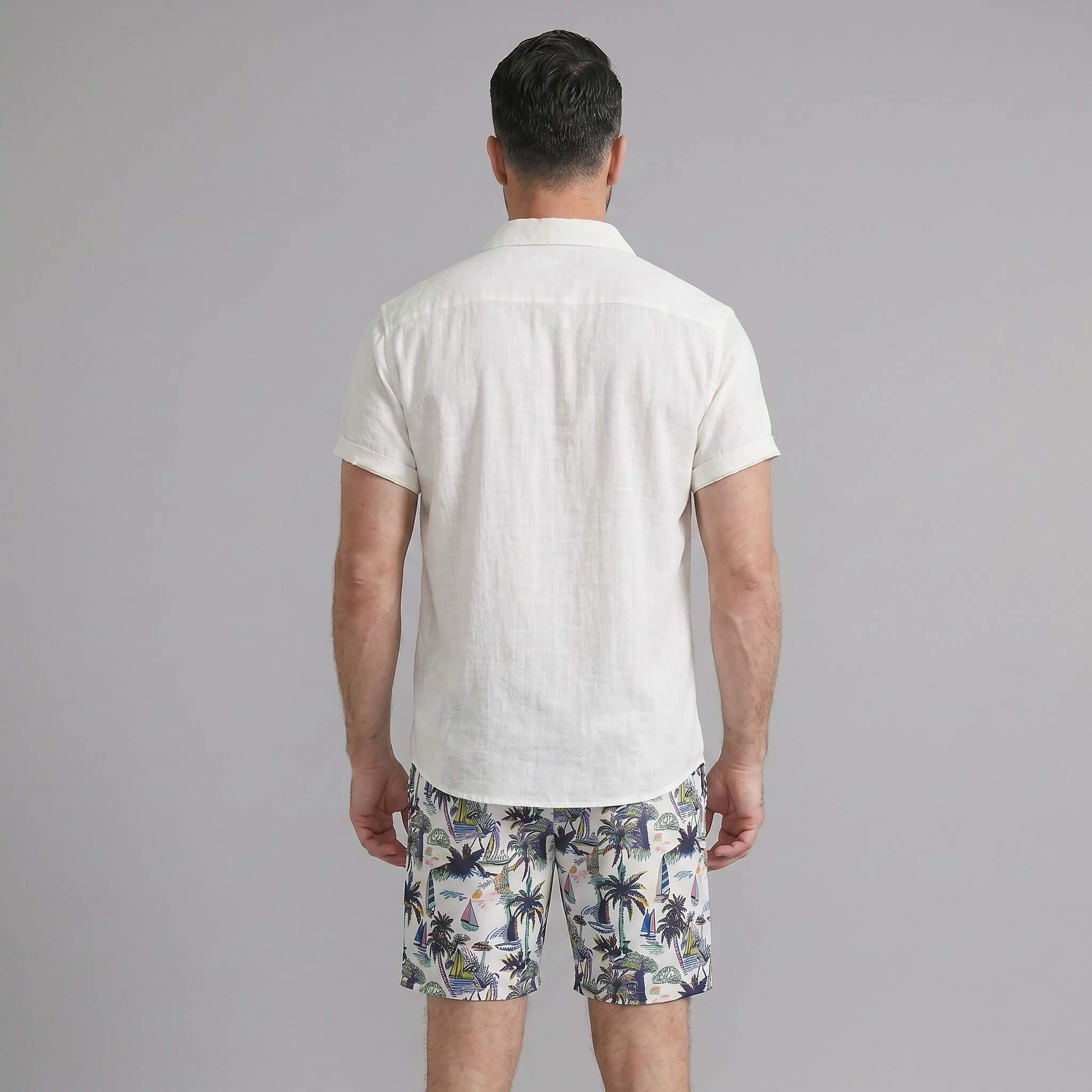Back view of man wearing black linen rayon shirt and white palm tree print swim shorts