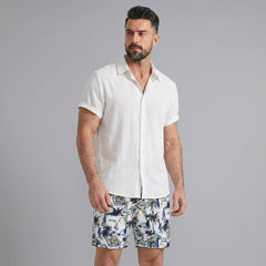 Man wearing a black linen rayon button up shirt and white palm tree print swim shorts front view