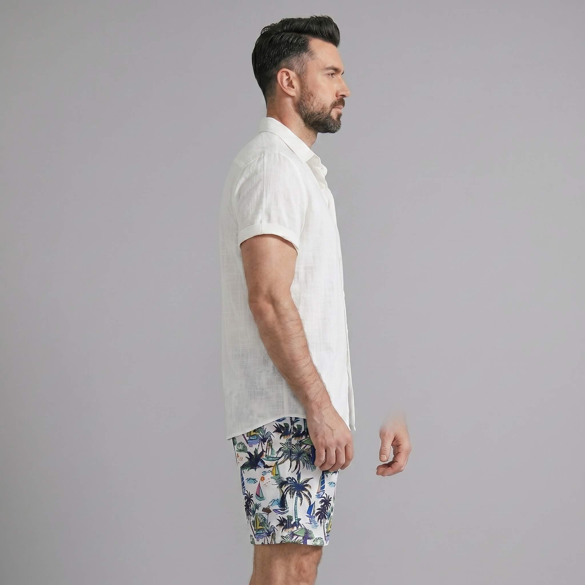 Side view of man in black linen rayon button up shirt and white palm tree print swim shorts