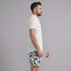 Side view of man in black linen rayon button up shirt and white palm tree print swim shorts