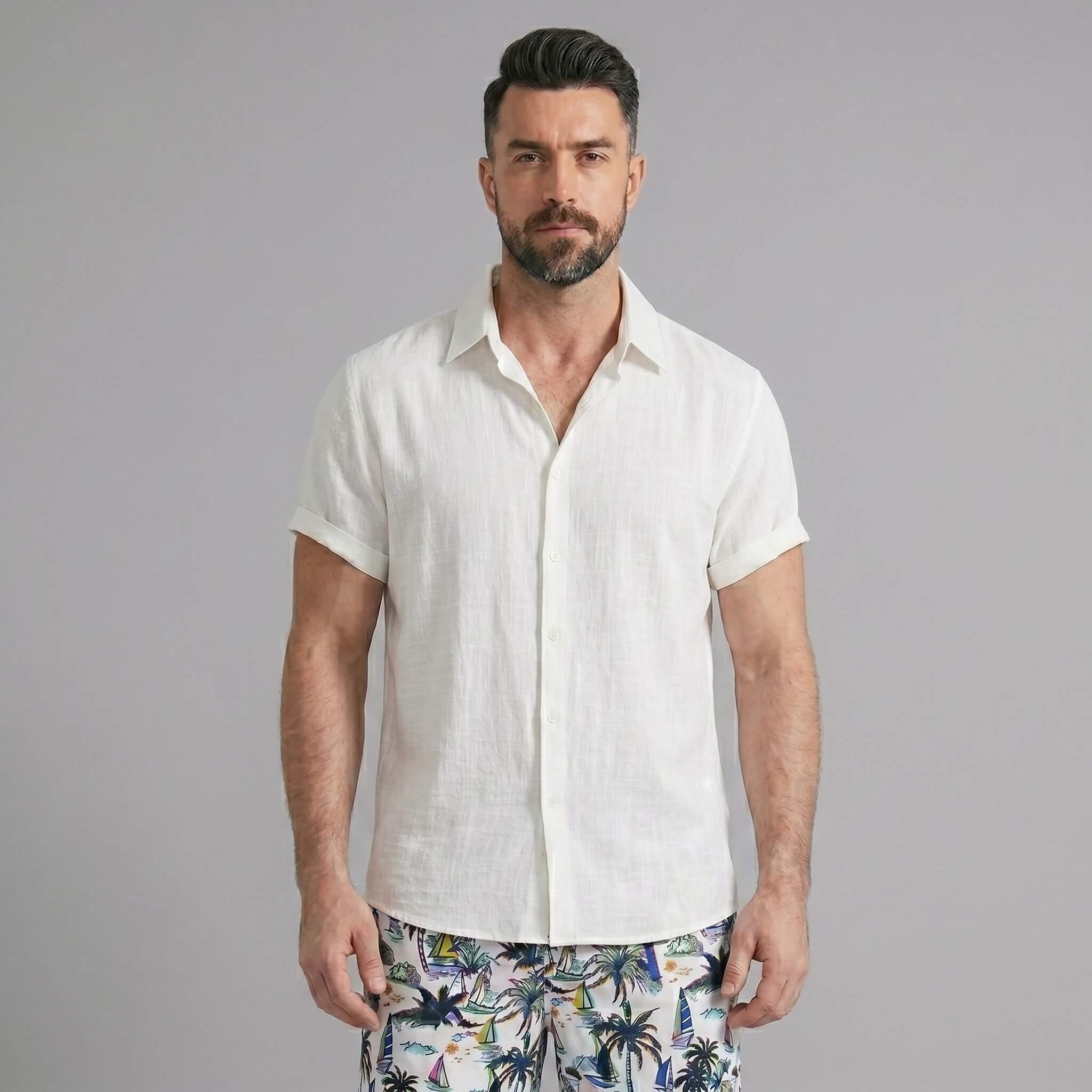Three quarter view of man in black linen rayon shirt and white palm tree print swim shorts