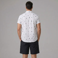 Side view of man in black palm tree anchor sailboat print shirt and swim shorts on plain background