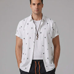 Three quarter view of man in black palm tree anchor sailboat print shirt and swim shorts