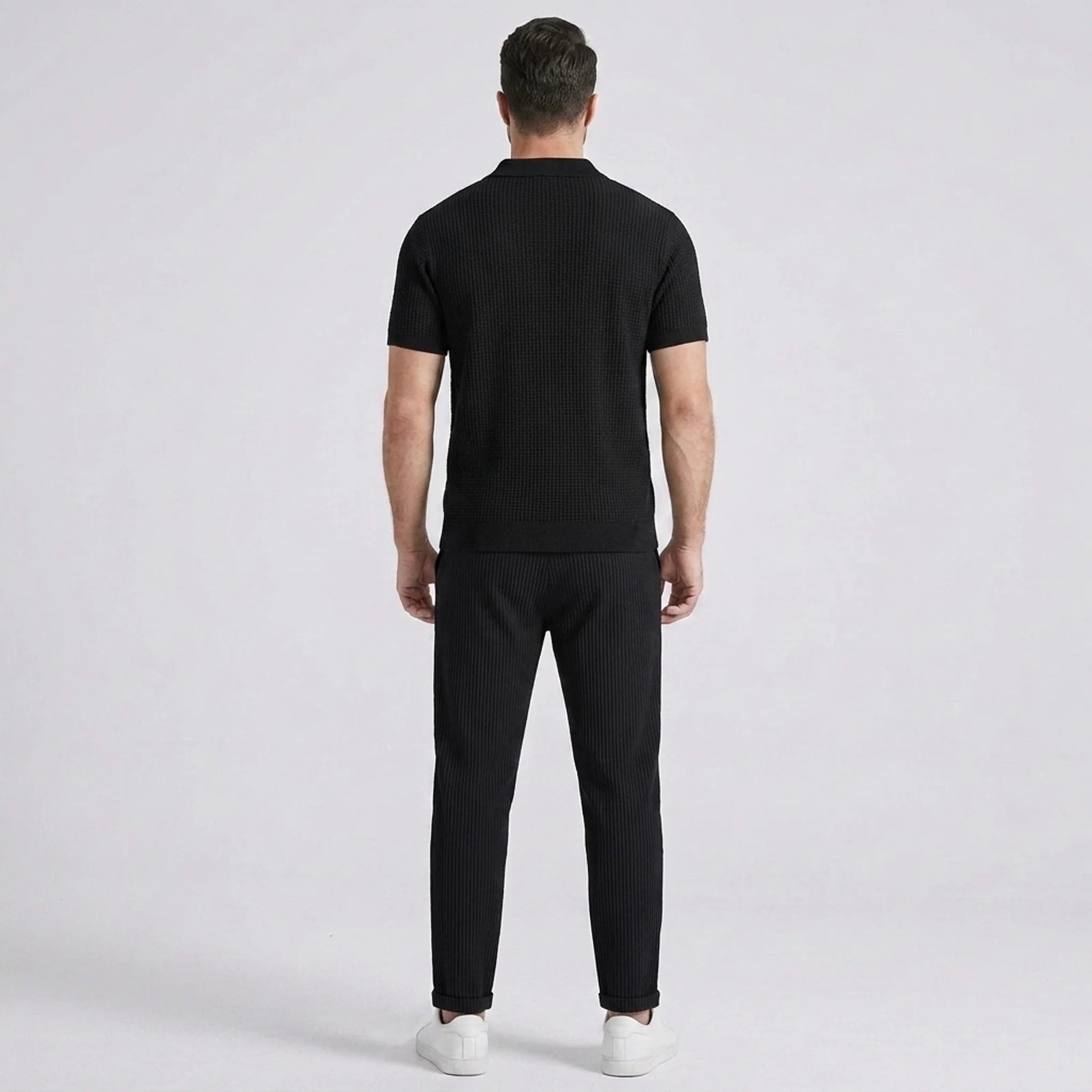 Three quarter view of man in black striped knit polo and waffle drawstring pants outdoors