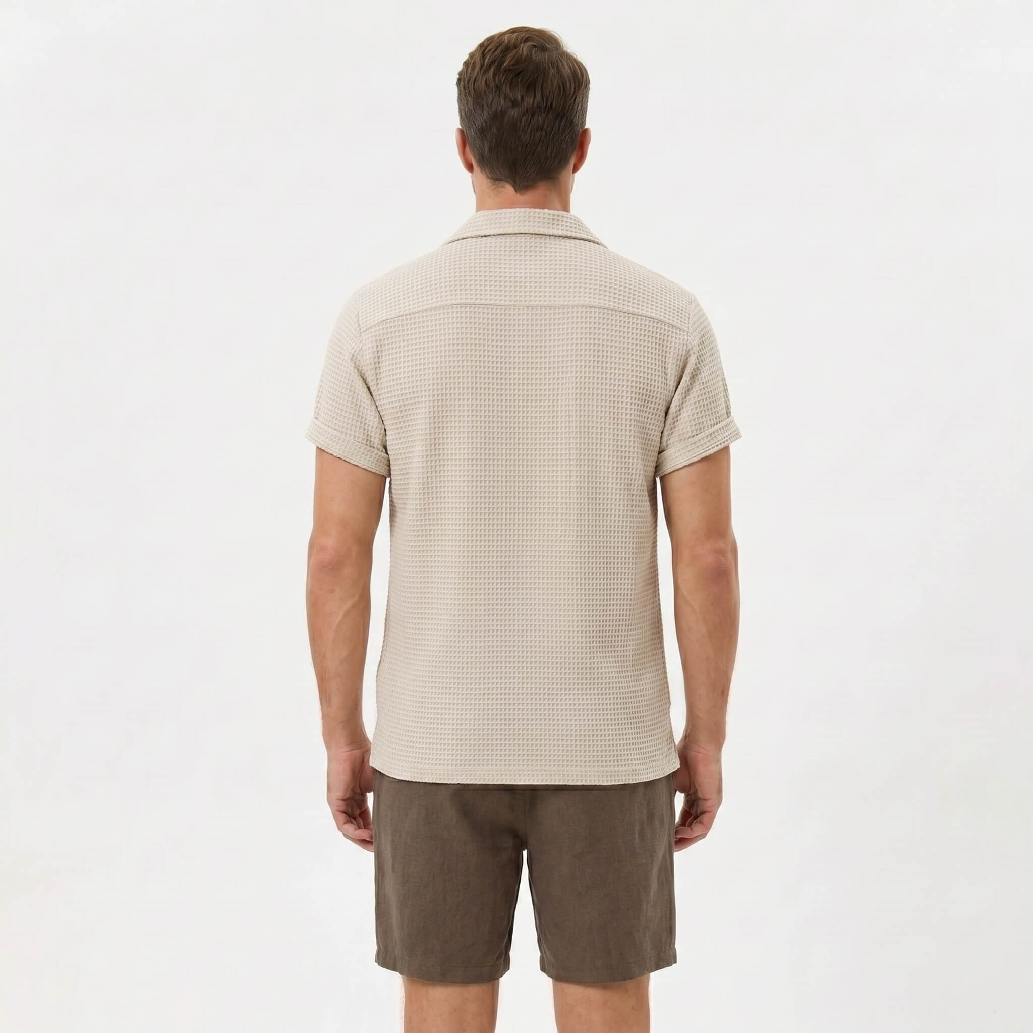 Side view of man in black textured Cuban shirt and linen cotton drawstring shorts on plain background