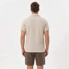 Side view of man in black textured Cuban shirt and linen cotton drawstring shorts on plain background