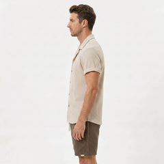 Three quarter view of man in black textured Cuban shirt and linen drawstring shorts on plain background