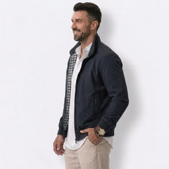 Man wearing MannerCo blue solid bomber jacket with stand collar, side view on plain background