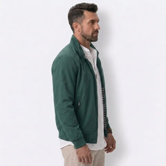 Man wearing MannerCo green solid bomber jacket with stand collar, side view on plain background