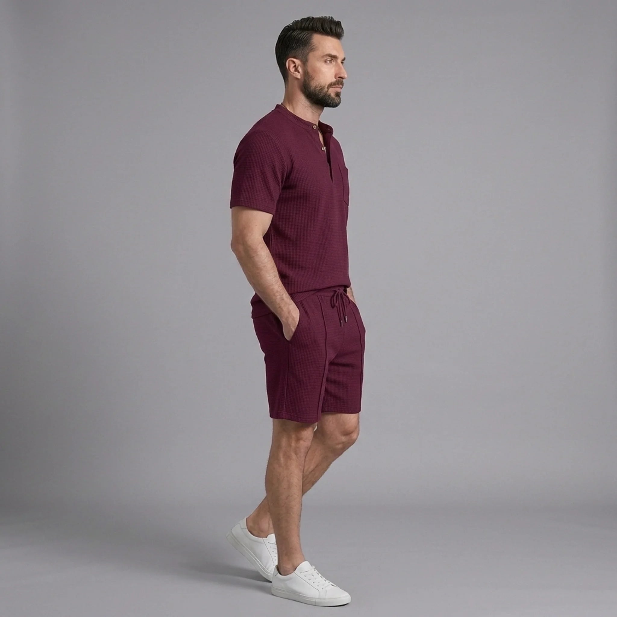 Side view of man in claret waffle stand collar shirt and drawstring shorts on plain background