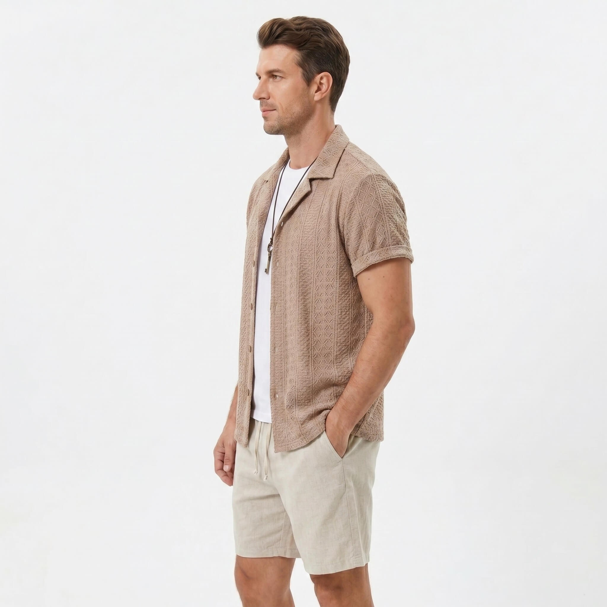Side view of man in coffee brown floral checkerboard jacquard Cuban shirt and linen drawstring shorts