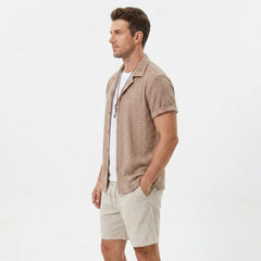 Side view of man in coffee brown floral checkerboard jacquard Cuban shirt and linen drawstring shorts