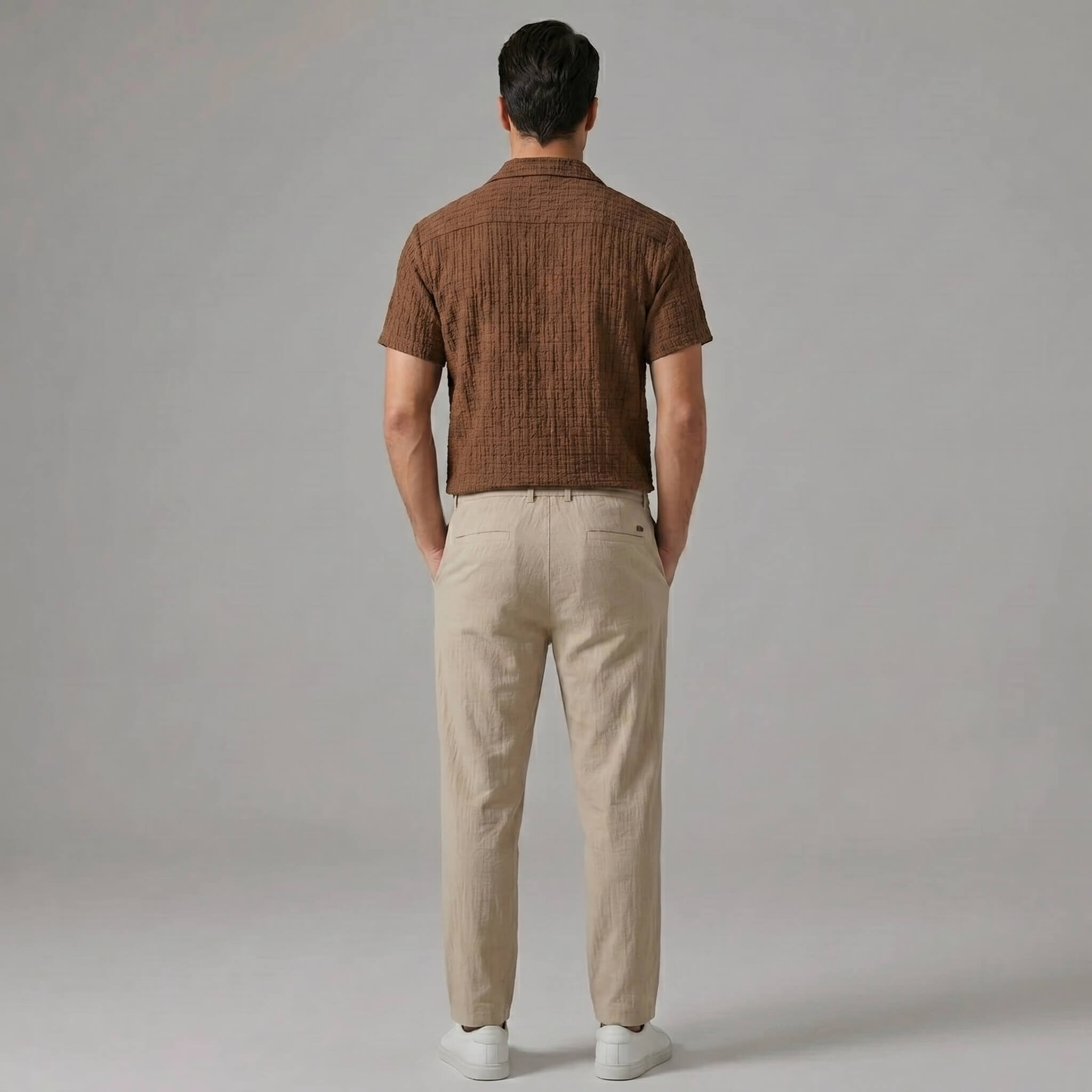 Back view of man wearing coffee brown jacquard Cuban collar shirt and crinkle textured straight leg pants