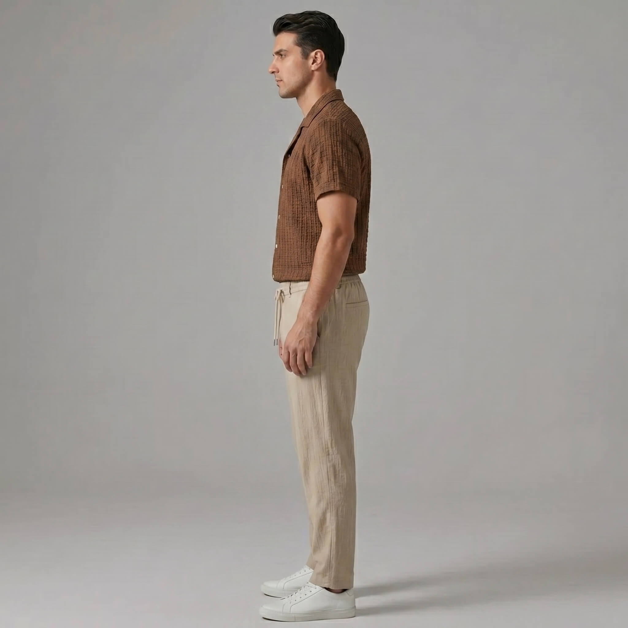Side view of man in coffee brown jacquard Cuban shirt and crinkle straight leg pants on plain background