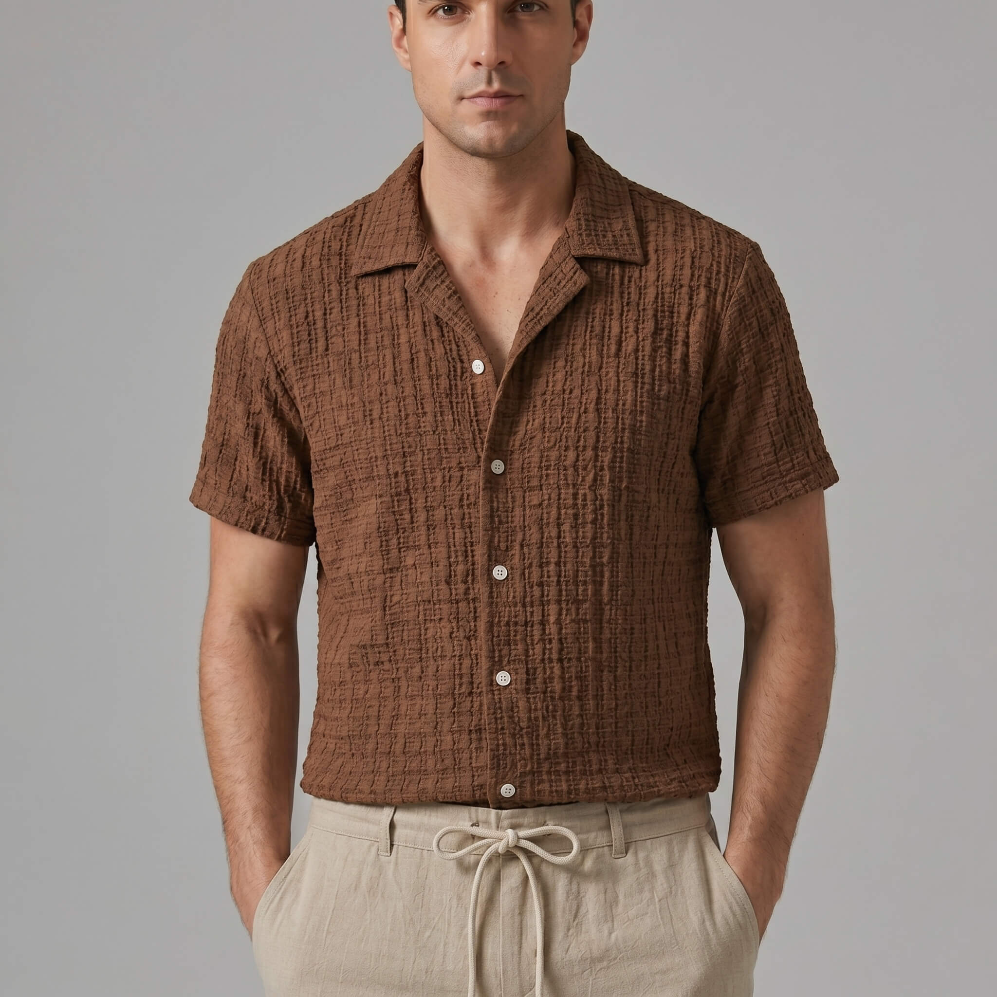 Three quarter view of man in coffee brown jacquard Cuban shirt and crinkle pants on white background