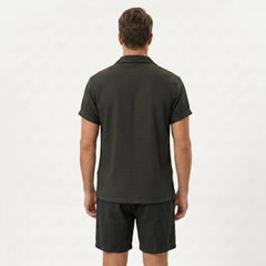Side view of man in coffee brown textured Cuban shirt and linen drawstring shorts on plain background