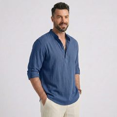 Man wearing MannerCo denim blue cotton linen long sleeve Henley shirt, side view on plain background