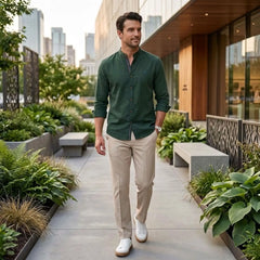 Man wearing dark green linen stand collar shirt with beige slim tapered trousers walking outdoors