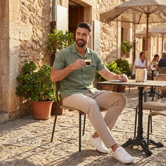 Man in dark green linen Cuban collar shirt and slim fit tapered trousers walking in sunny outdoor summer scene
