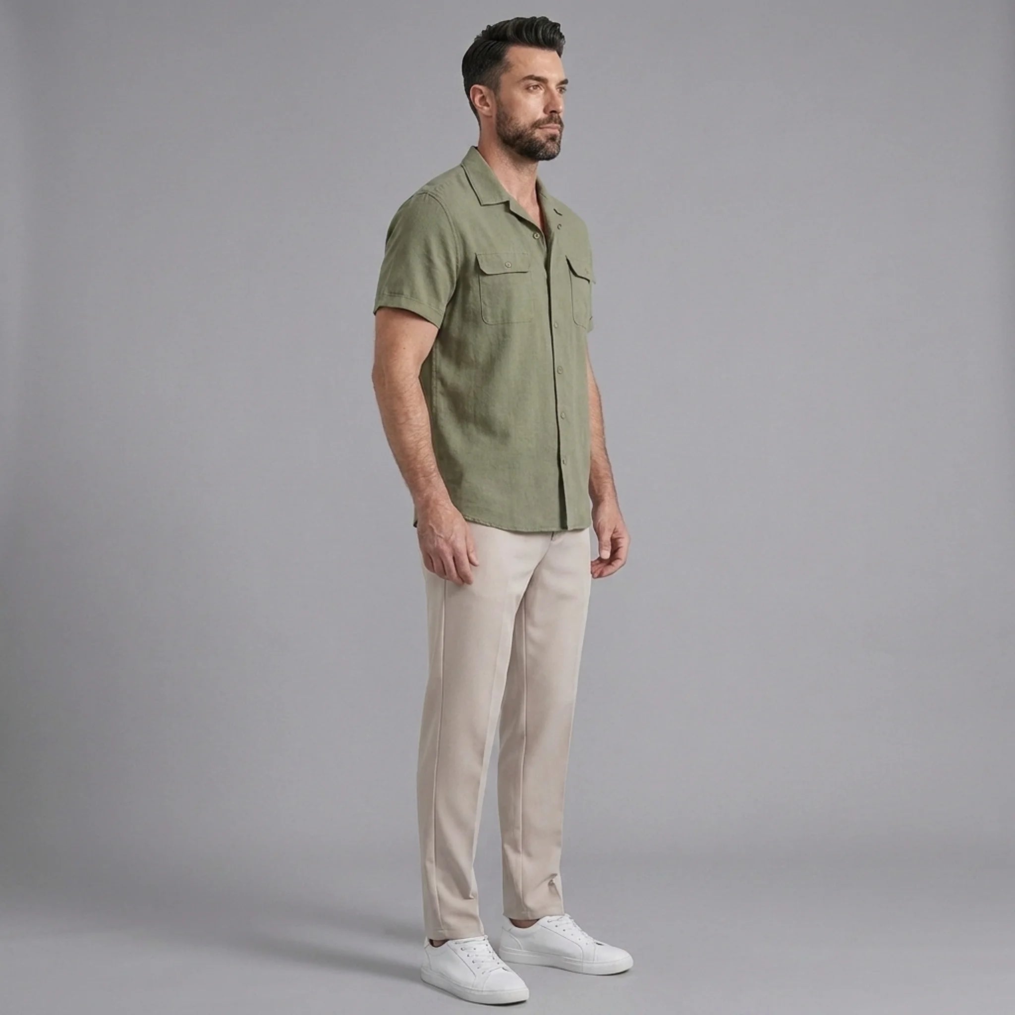 Side view of man in dark green linen Cuban collar shirt and slim fit tapered trousers on plain background