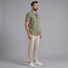 Side view of man in dark green linen Cuban collar shirt and slim fit tapered trousers on plain background