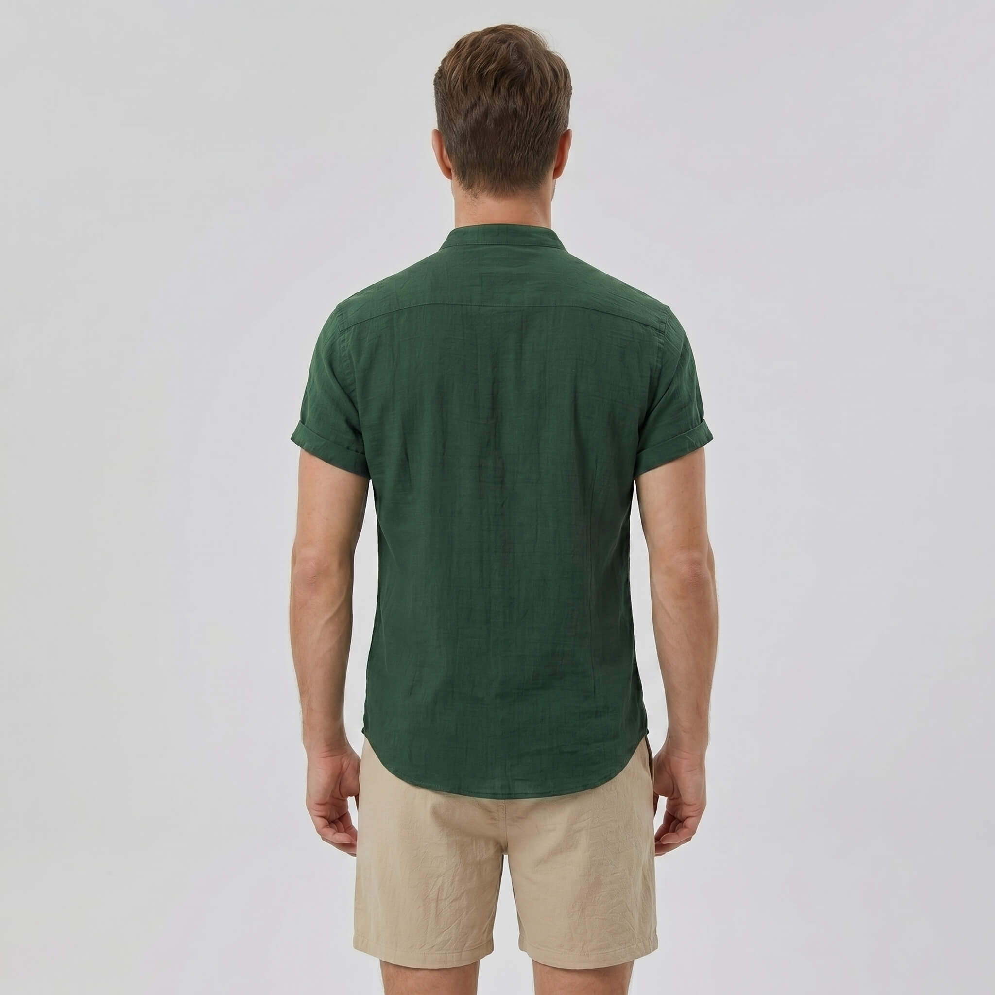 Back view of man wearing dark green linen look stand collar shirt and crinkle drawstring shorts