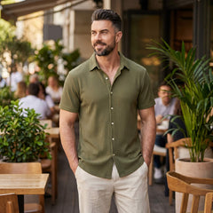 Man wearing dark green waffle button up shirt and linen pants relaxed in outdoor setting