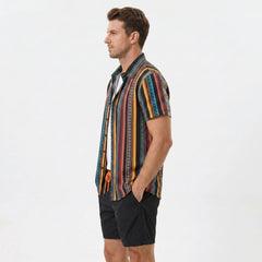 Side view of man in ethnic geometric print button up shirt and swim shorts on plain background