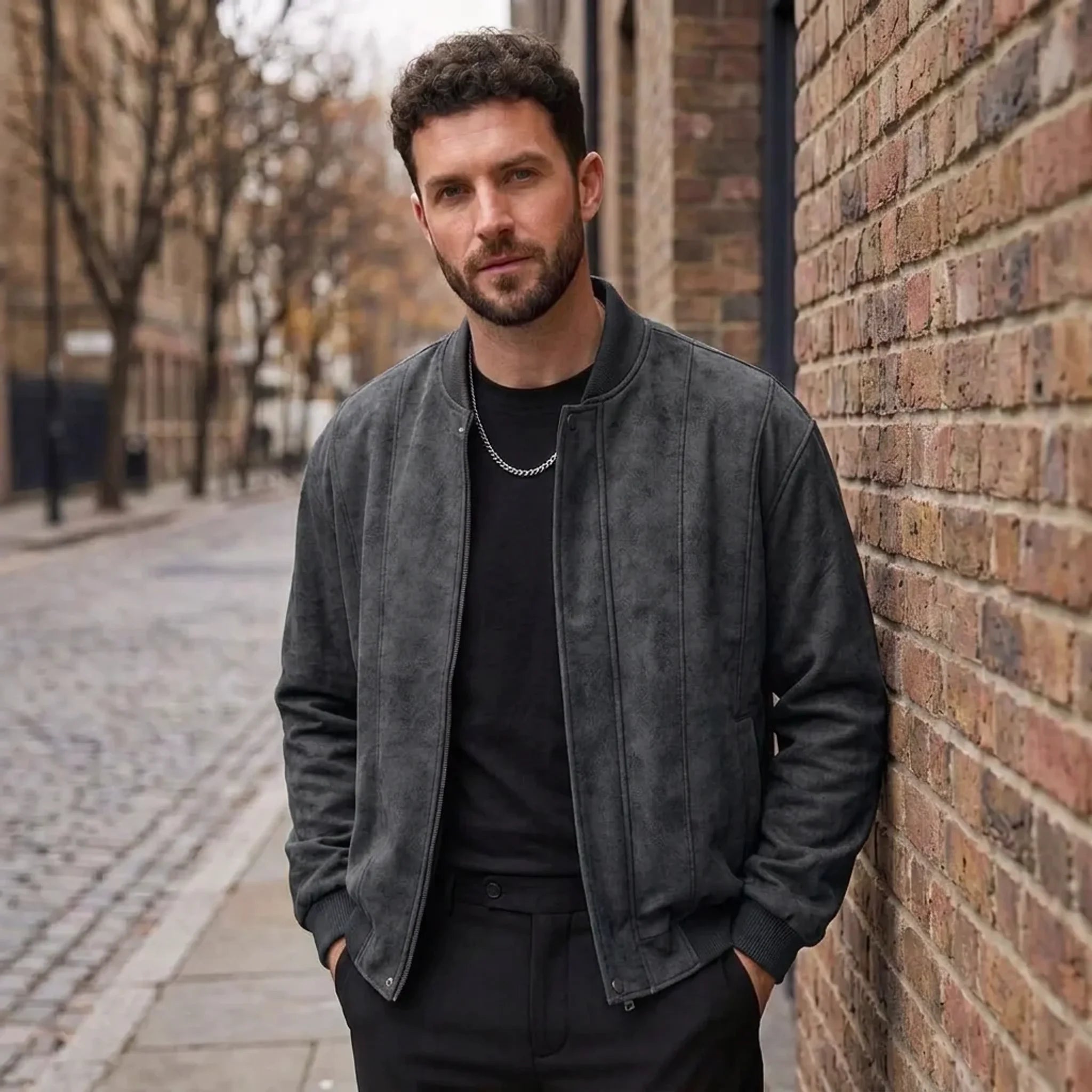 MannerCo men's faux suede bomber jacket in black worn open over black tee on cobblestone street