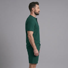 Side view of man in green waffle stand collar shirt and drawstring shorts on plain background