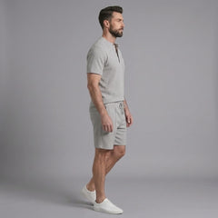 Side view of man in grey waffle stand collar shirt and drawstring shorts on plain background
