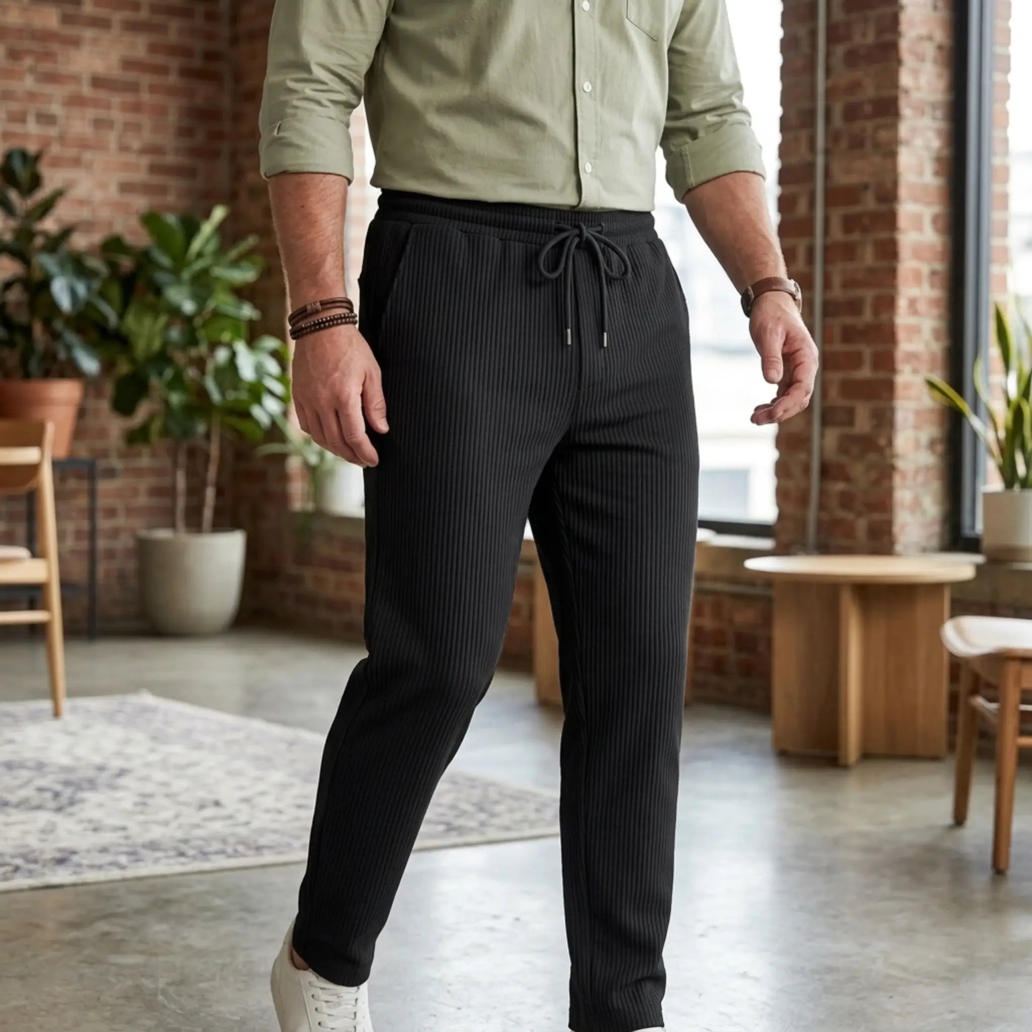 Man wearing MannerCo black jacquard ribbed straight leg drawstring trousers, side view on plain background