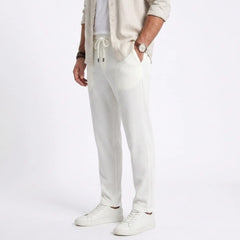 Man wearing MannerCo white jacquard ribbed straight leg drawstring trousers, side view on plain background