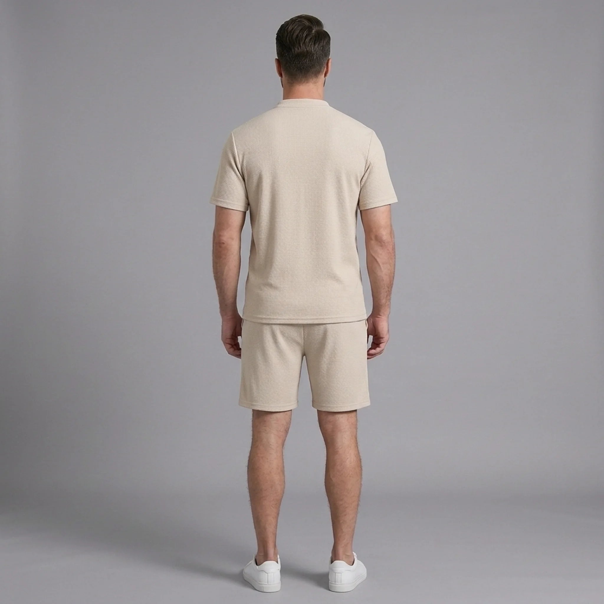 Side view of man in khaki waffle stand collar shirt and drawstring shorts on plain background
