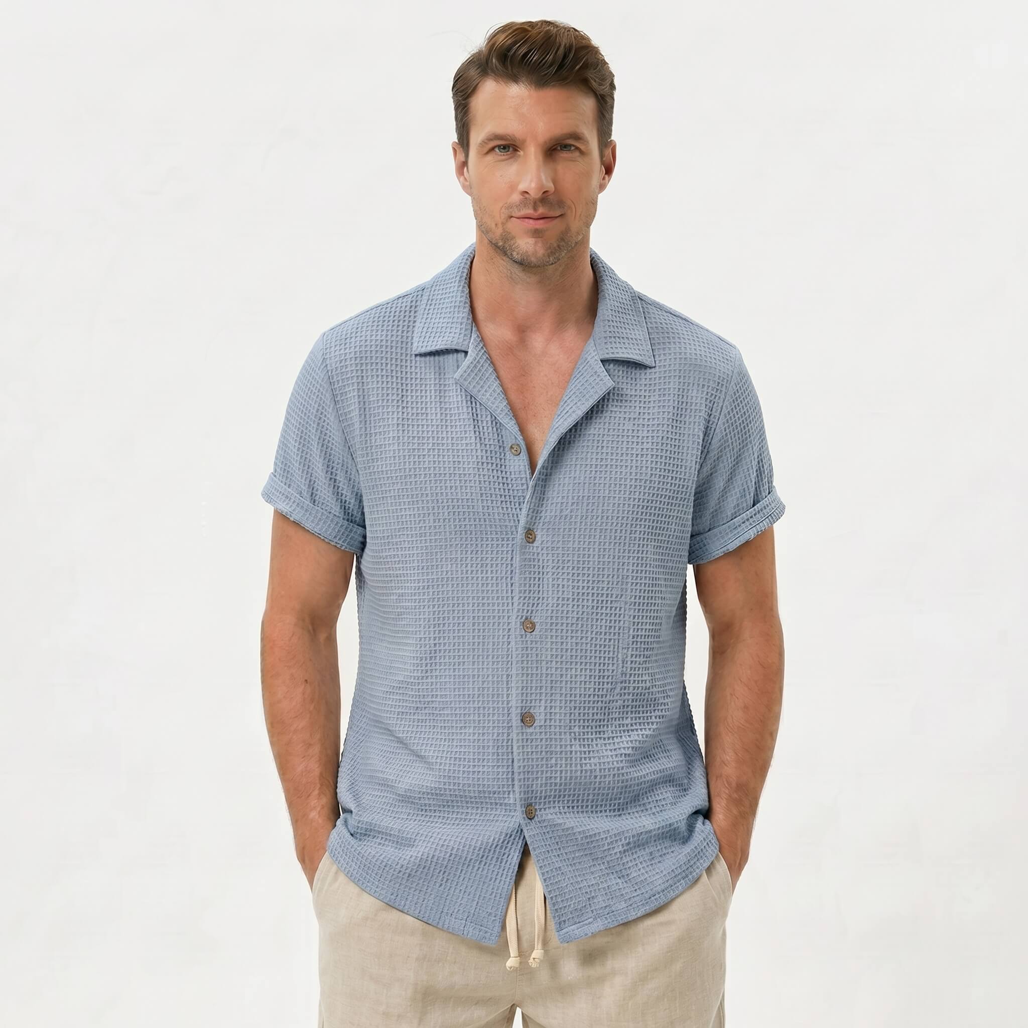Three quarter view of man in light blue textured Cuban shirt and drawstring shorts on plain background