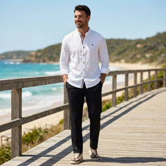 Man wearing white linen stand collar shirt and black slim fit trousers on sunny beach boardwalk