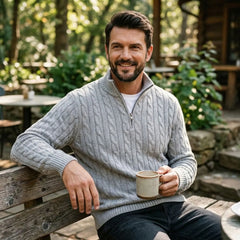 Man in light grey cable knit quarter-zip sweater seated outdoors