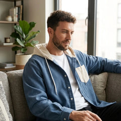 Man in denim blue corduroy hooded shirt jacket seated on a sofa at home