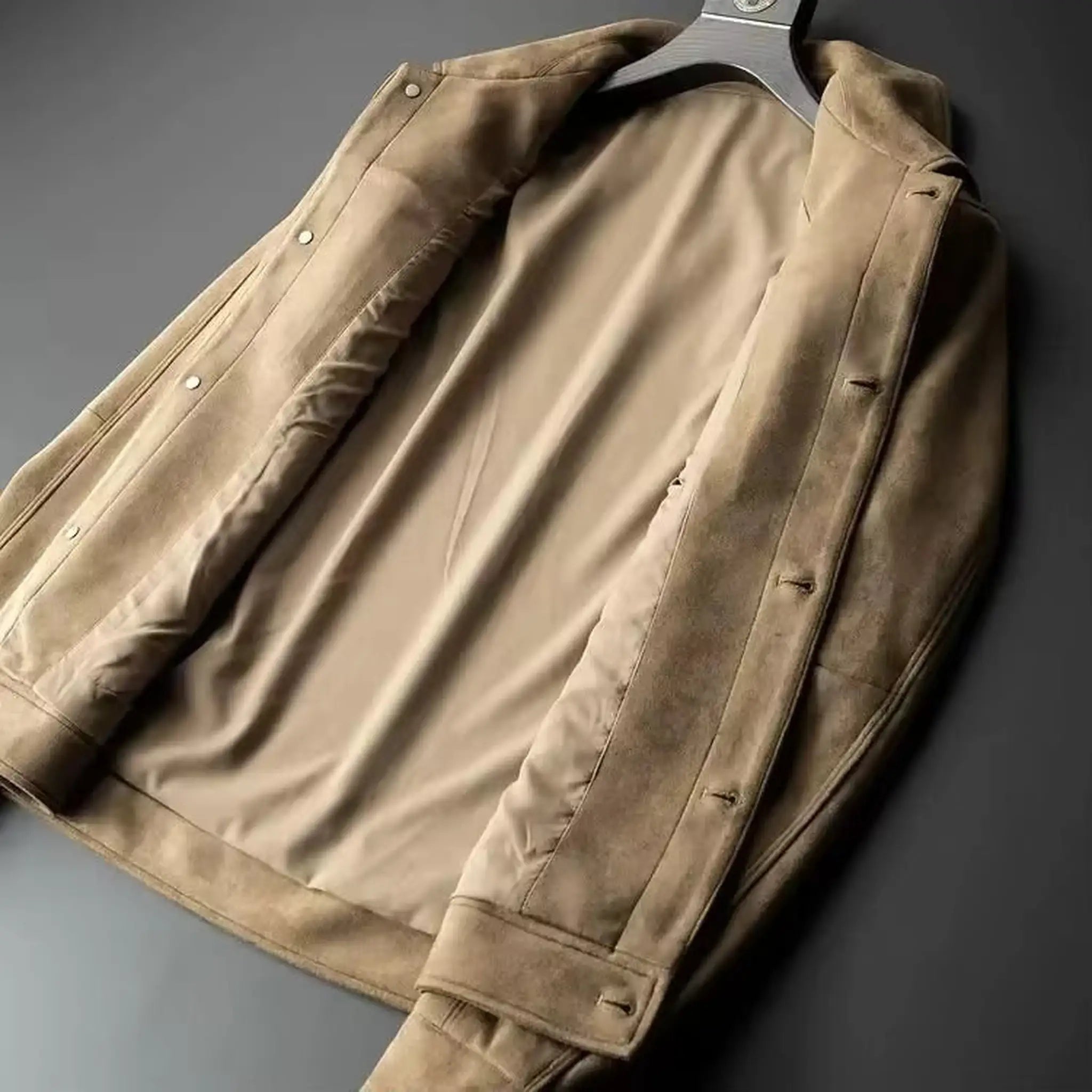 Khaki suede-look trucker jacket laid open on a dark surface to show the smooth inner lining