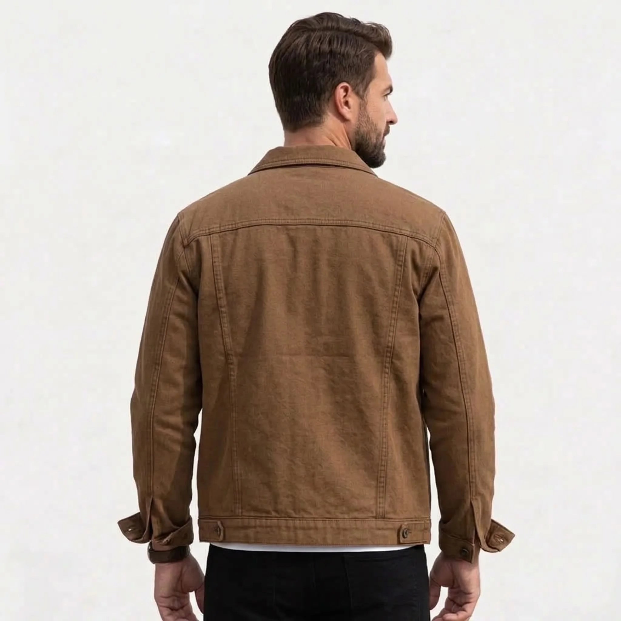 A man viewed from the back wearing a coffee canvas utility jacket, paired with black pants, against a plain off-white background.
