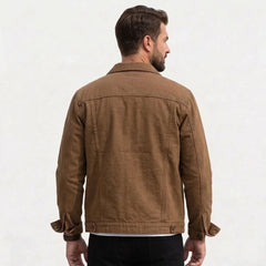 A man viewed from the back wearing a coffee canvas utility jacket, paired with black pants, against a plain off-white background.