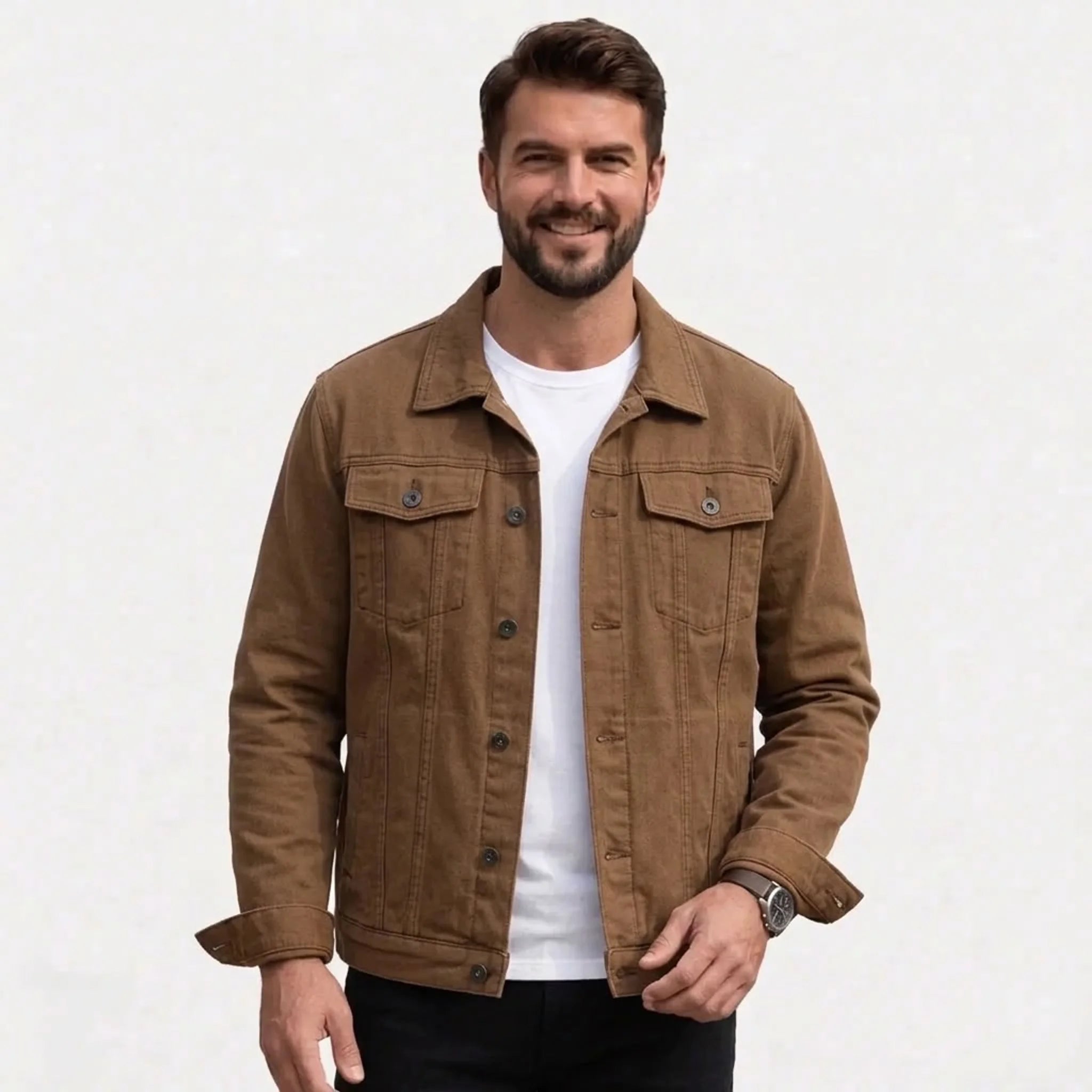 A smiling man wearing a coffee button-up trucker jacket over a white t-shirt and black pants, photographed against a clean white studio background.